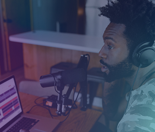 Person at desk speaking into studio mic with laptop nearby