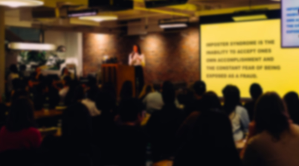 Blurred image of speaker presenting on stage in dark room