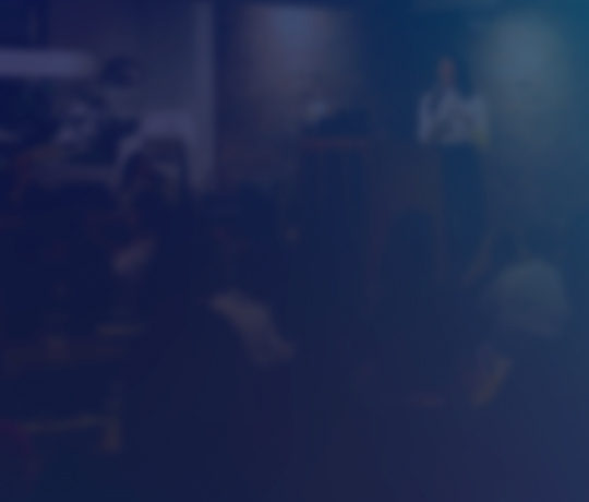 Blurred image of speaker presenting on stage in dark room