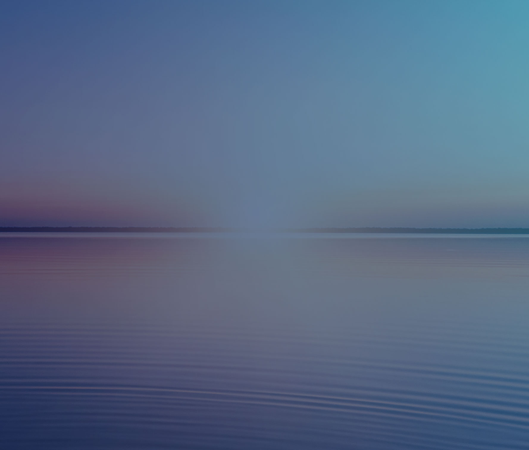 Tranquil sunset over calm water with a bright sun on the horizon, creating a symmetrical reflection and gradient from deep blue to soft pink and orange hues in the sky